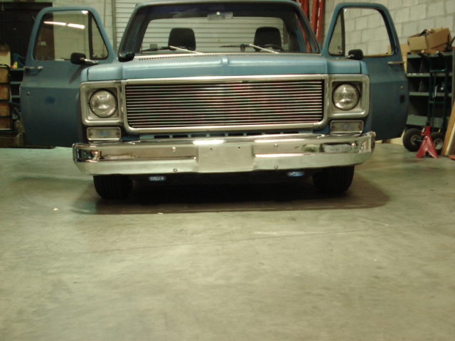 Front view of a light blue pickup truck with doors open. It has a chrome bumper and a horizontal grille