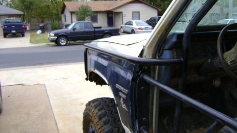 1986 Ford Bronco - Stripped blue Bronco with the doors, windshield glass and interior trim removed, showing a black tube cage/A-pillar hoop, bare dash and ste…