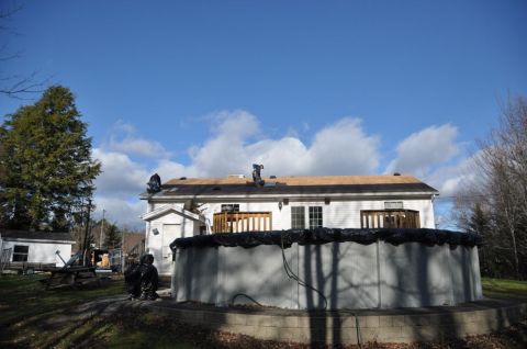 1996 Ford Bronco - Workers are seen on the roof of a house, performing repairs under a partly cloudy sky, with an above-ground pool in the foreground.