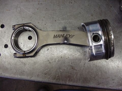 2007 Ford Mustang - Close-up of a Manley connecting rod and piston assembly on a workbench.