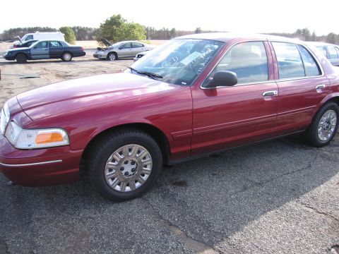 2001 Ford Crown Victoria - A red sedan is parked in an outdoor lot with other vehicles visible in the background.