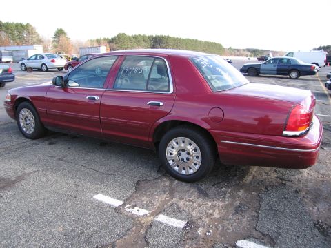 2001 Ford Crown Victoria - A red 2001 Ford Crown Victoria sedan is parked in an outdoor lot, viewed from the side.