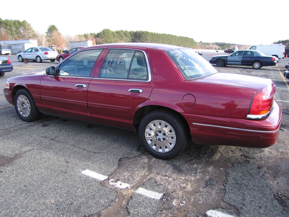 Red 2001 Ford Crown Victoria sedan, side view, with a number 197853 written on the driver's side window