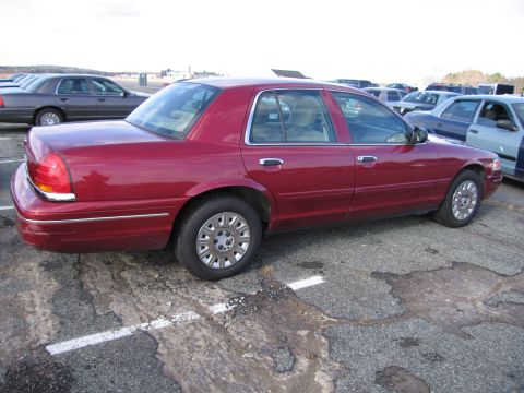 2001 Ford Crown Victoria - A red Ford Crown Victoria is parked in a lot with other vehicles visible in the background.