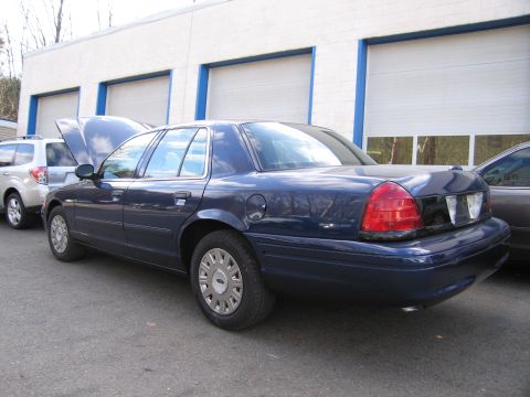 1991 Ford LTD Crown Victoria - A dark blue sedan is parked in front of a commercial building with its hood open, next to a white SUV.