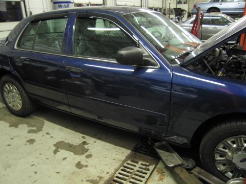 1991 Ford LTD Crown Victoria - A blue sedan is parked in a garage with its hood open, resting on a lift over a floor drain.
