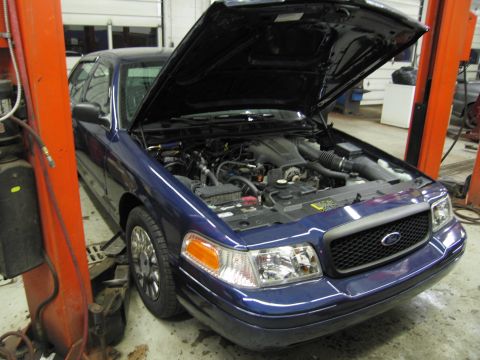 1991 Ford LTD Crown Victoria - The front end of a blue Ford Crown Victoria is visible with its hood raised, revealing the engine compartment.
