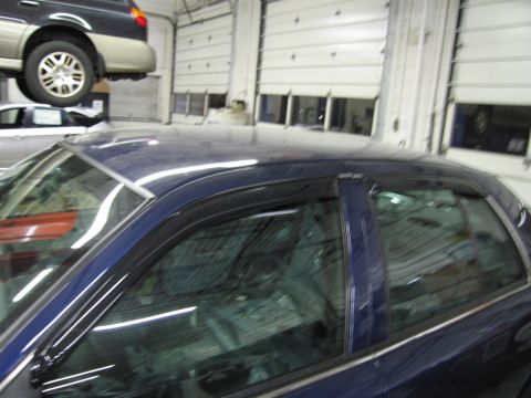 1991 Ford LTD Crown Victoria - A dark blue sedan is parked in a garage, with another vehicle raised on a lift above it.