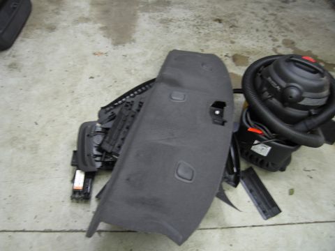 1991 Ford LTD Crown Victoria - A disassembled gray interior car panel lies next to a black shop vacuum on a concrete floor.