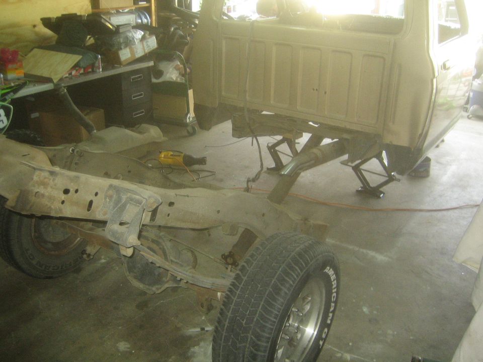 Tan pickup cab raised on scissor jacks with frame pulled forward in a garage