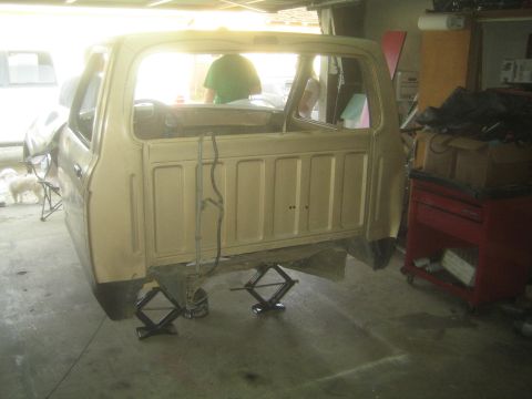 1990 Ford Bronco - rear of a tan truck cab sits on scissor jacks in a garage, with a person visible through the back window and a red tool chest nearby.