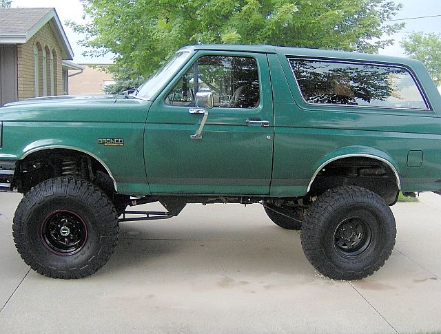 Green 1990 Ford Bronco with lifted suspension and large tires, side view