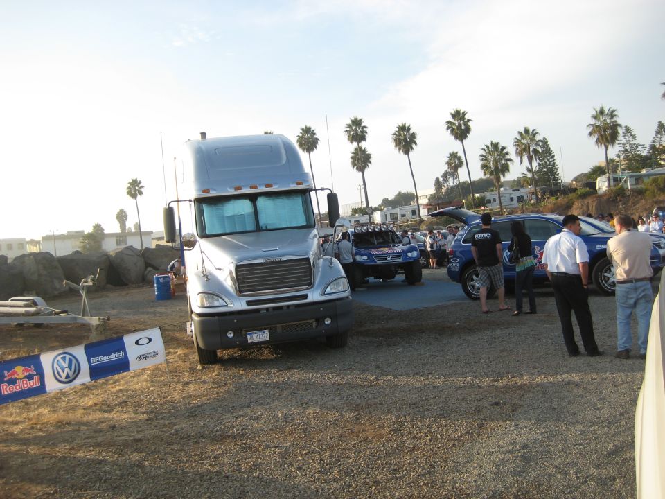 Silver semi-truck parked next to a blue off-road vehicle and a blue SUV