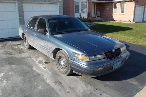 1985 Mercury Grand Marquis - This blue sedan, likely a 1995 model, is parked in a driveway with a house and garage in the background.