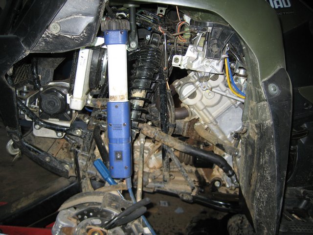 Close-up of ATV engine, shock absorber, and suspension parts. Some wiring and hoses are visible