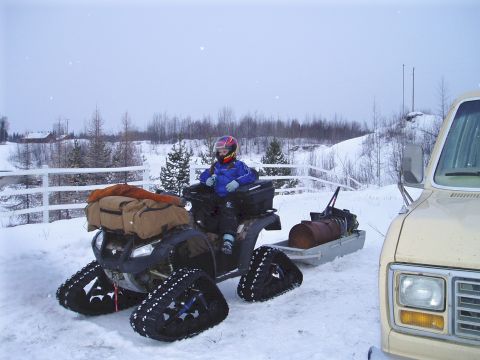 2000 Ford E350 - A person rides an ATV equipped with tracks and a trailer in a snowy environment next to a van.