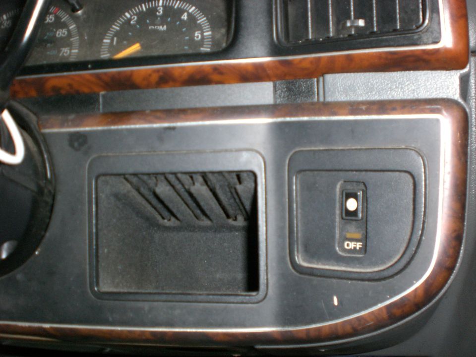 Black dashboard with woodgrain trim, open storage pocket, OFF switch, and gauges above