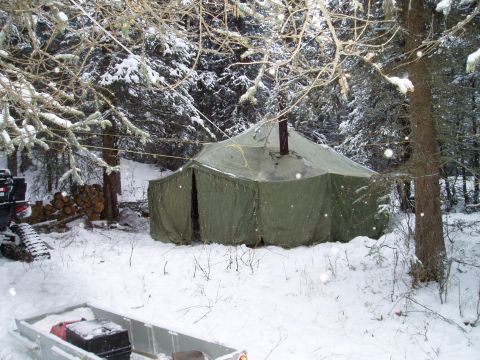 2000 Ford E350 - A winter camp scene with a tent, firewood, and a trailer in a snow-covered forest.