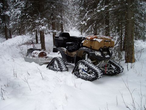2000 Ford E350 - An all-terrain vehicle equipped with tracks is parked in a snowy forest next to a sled.