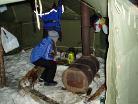 2000 Ford E350 - A person sits inside a tent next to a wood-burning stove, with snow on the ground.