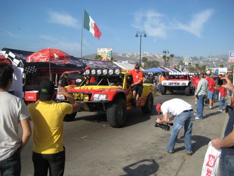 1996 Ford Bronco - Off-road trucks and spectators gather under a bright blue sky with a Mexican flag overhead.