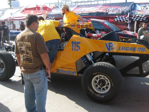 1996 Ford Bronco - A yellow off-road truck with racing decals is parked at an event, with people around it.