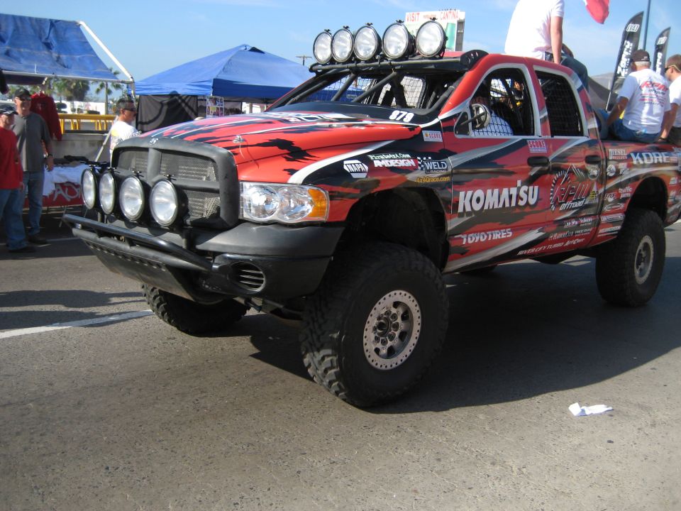 Off-road race truck with lights on roof and bumper, red and black graphics, Komatsu and Toyo Tires logos