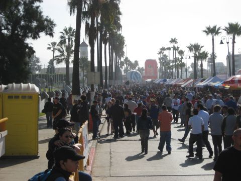 1996 Ford Bronco - A large crowd walks down a street lined with palm trees and vendor tents.