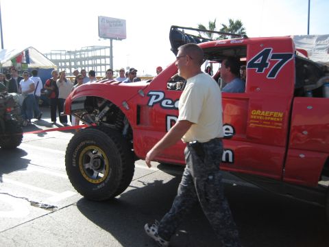 1996 Ford Bronco - A red off-road racing truck is seen with spectators and a billboard in the background.