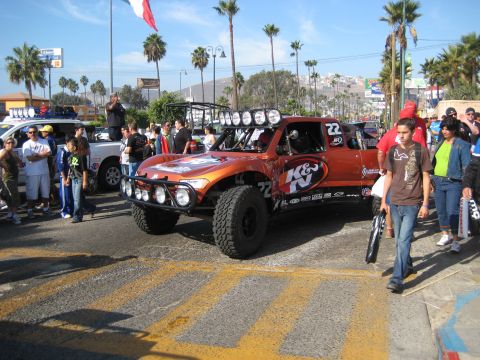 1996 Ford Bronco - An orange off-road race truck with multiple lights on the roof and bumper is seen with spectators.