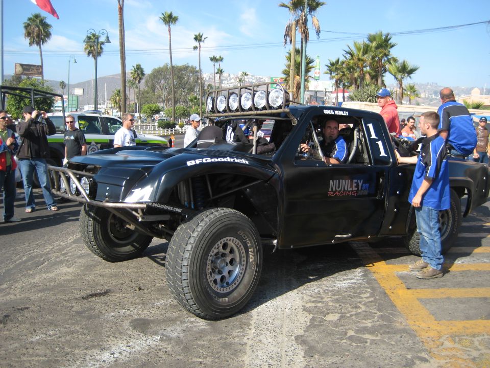 Black off-road racing truck with BFGoodrich tires and a roll cage, parked on a street