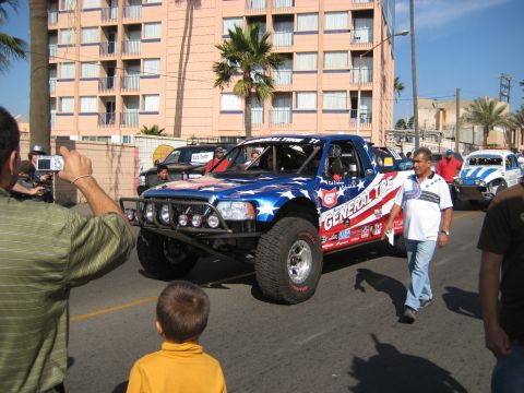1996 Ford Bronco - This off-road truck, adorned with General Tire branding and an American flag motif, is seen on a street with spectators and other vehicles.