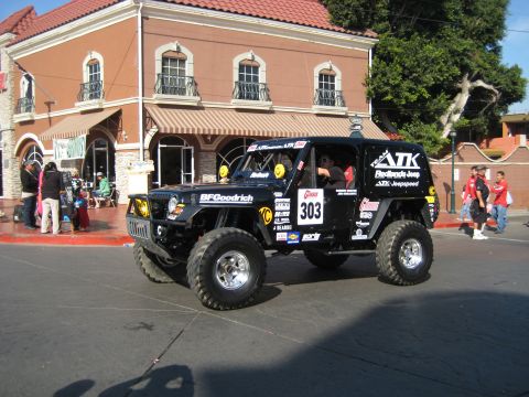 1996 Ford Bronco - A modified Jeep Wrangler with racing decals drives past a building with awnings.
