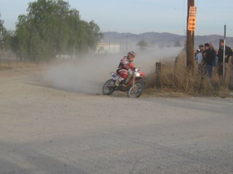 1996 Ford Bronco - A motorcycle racer speeds around a dusty corner, with a small group of onlookers nearby.