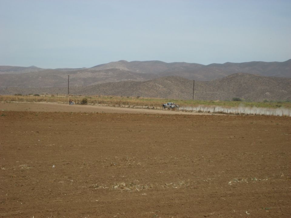 Off-road race truck kicking up dust on a dirt road with mountains in the background