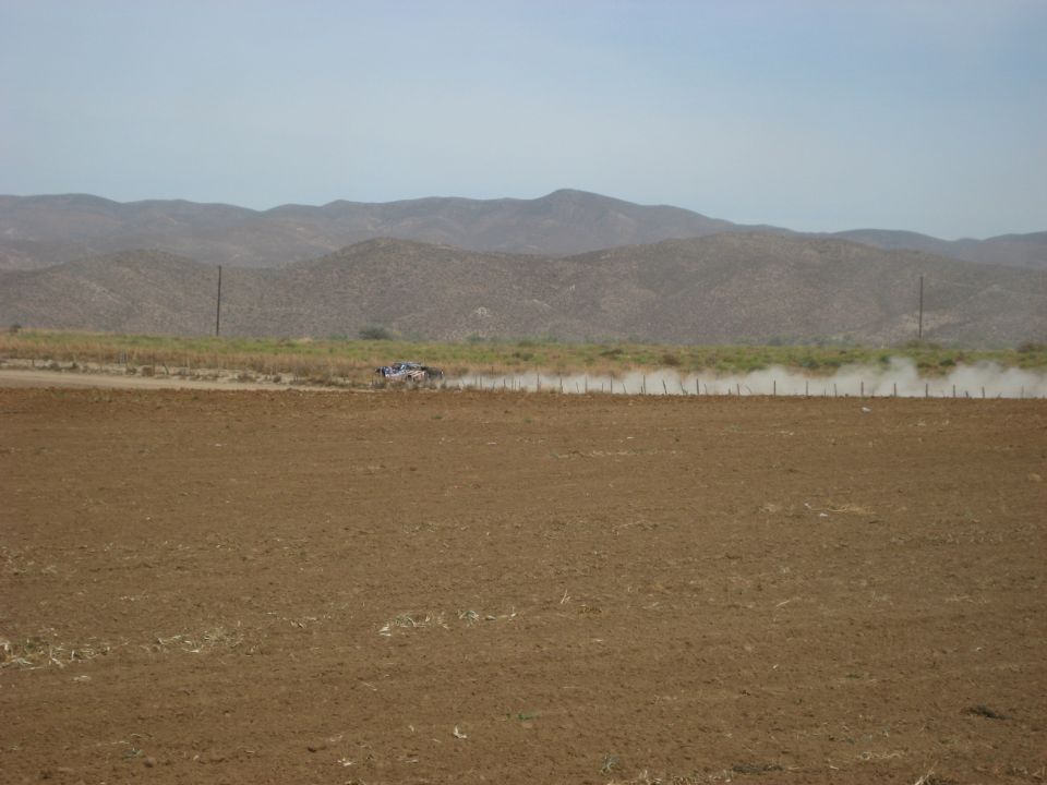 Off-road vehicle kicking up dust on a dirt road with mountains in the background