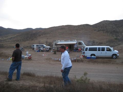 1996 Ford Bronco - A desert campsite is set up with multiple vehicles and an RV under a cloudy sky.