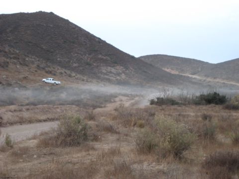 1996 Ford Bronco - A white pickup truck navigates a dusty trail through a dry, hilly landscape under an overcast sky.