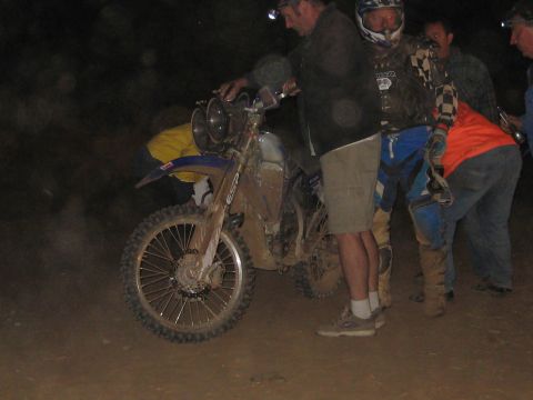 1996 Ford Bronco - A group of people gather around a dirt bike at night, likely during a race or event.