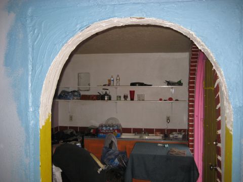 1996 Ford Bronco - A cluttered room interior is viewed through a blue and yellow arched doorway, revealing shelves stocked with items and a sink area.