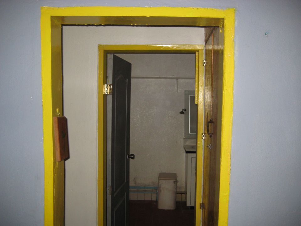 Interior doorway with bright yellow trim, showing an open dark door leading to a small room with a trash can