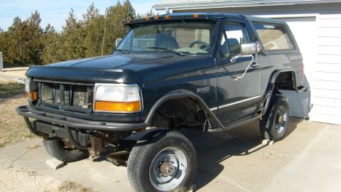 1995 Ford Bronco - This dark-colored Ford Bronco is parked in front of a garage, showing its modified front end and side profile.