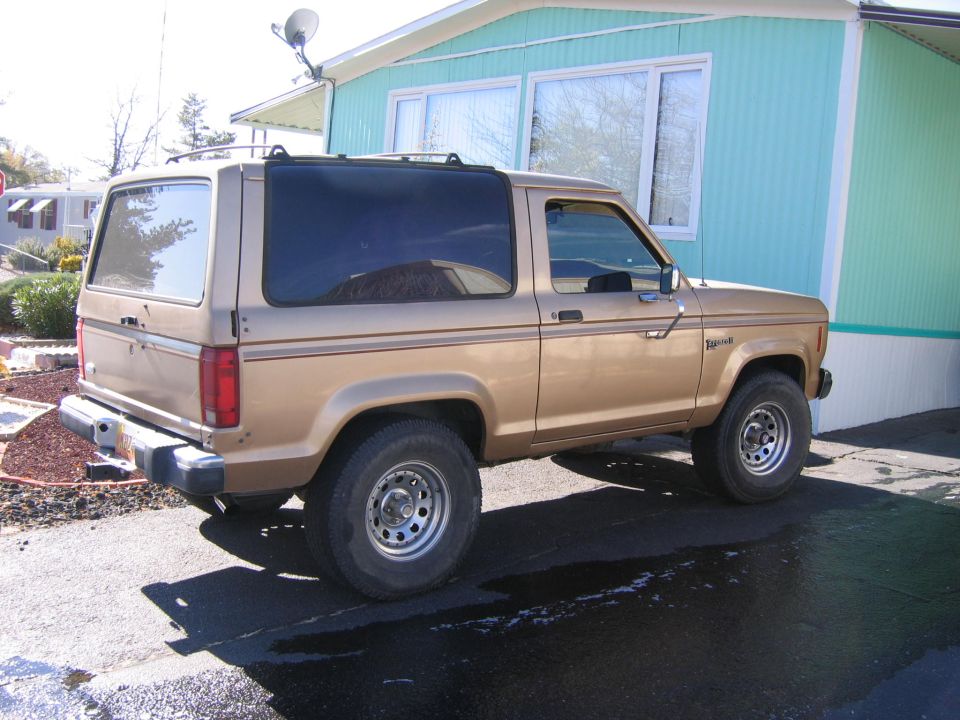 Gold 1984 Ford Bronco II parked in front of a teal and white mobile home