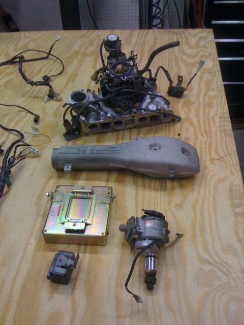 1987 Suzuki Samurai - Disassembled engine components, including an intake manifold and ECU, are arranged on a workbench.
