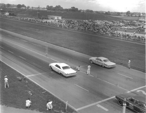 1963 Ford Galaxie - A drag race is underway with two cars speeding down the track and a crowd watching from the sidelines.