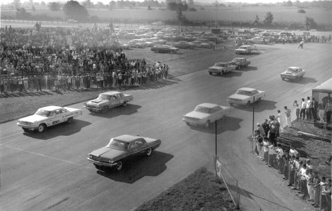 1963 Ford Galaxie - Multiple 1963 Ford Galaxies compete on a race track, observed by a crowd.