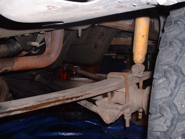 Underside view of a vehicle's rear axle and suspension components, including a yellow shock absorber and leaf springs