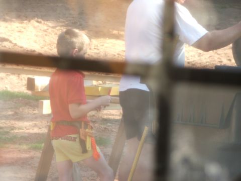 2005 Ford Mustang - A boy stands with a toy tool belt, while an adult is partially visible in the background.
