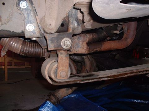 1983 Ford Bronco - Close-up of the undercarriage, focusing on suspension parts and rusted exhaust piping.