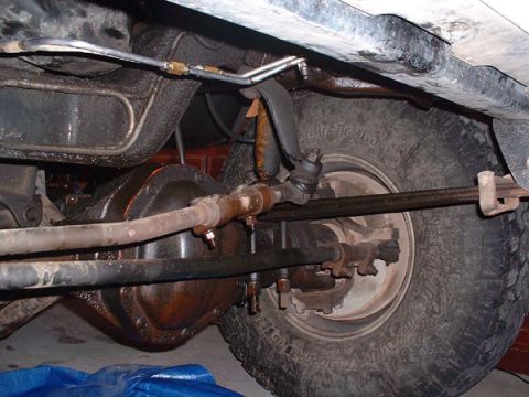 1983 Ford Bronco - Close-up of the front axle and steering components of a vehicle, with a tire and part of the undercarriage visible.